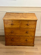 Wooden dresser with four drawers on a wooden floor against a white wall.