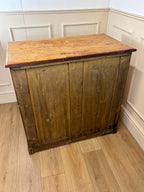 Wooden cabinet with a worn finish on a wooden floor against a white paneled wall.