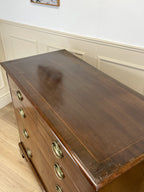 Wooden dresser with brass handles in a room with white walls and wooden floor.