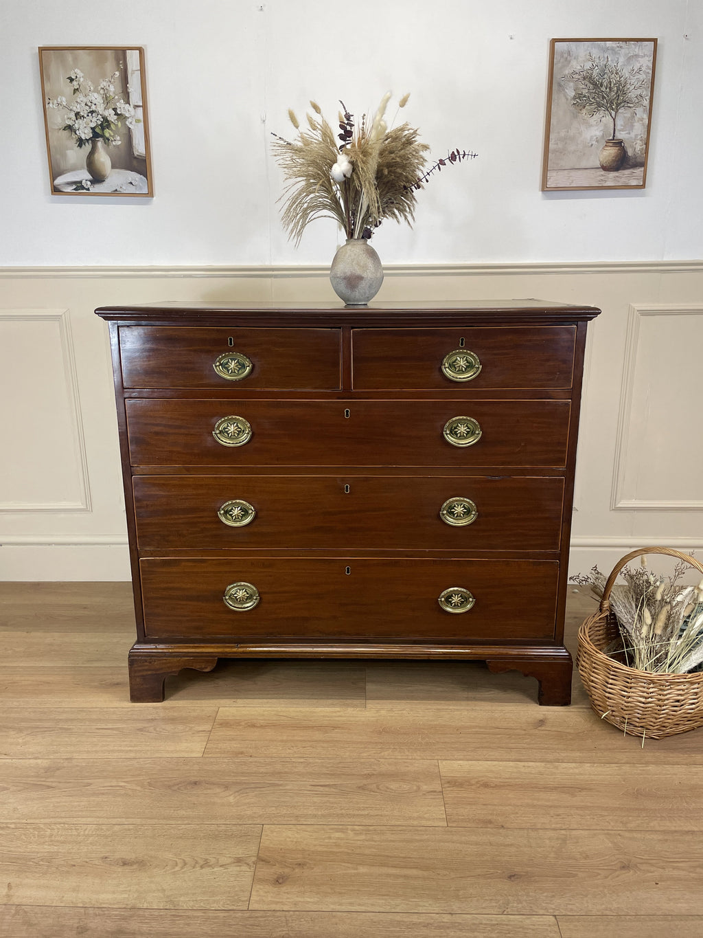 Wooden dresser with gold handles in a room with framed pictures on the wall.