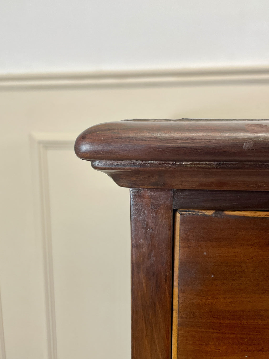 Close-up of a wooden cabinet corner with a neutral wall background