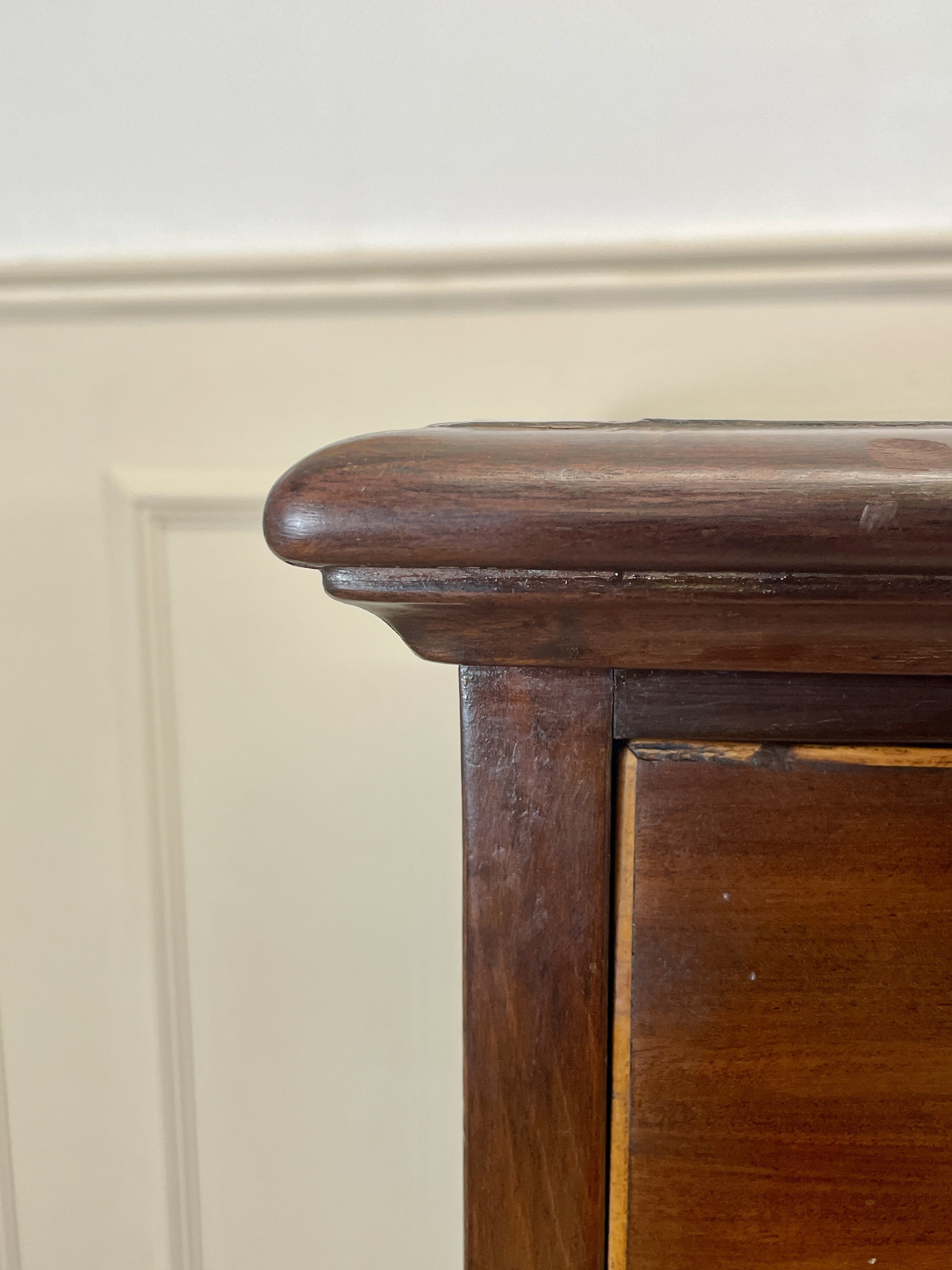 Close-up of a wooden cabinet corner with a neutral wall background