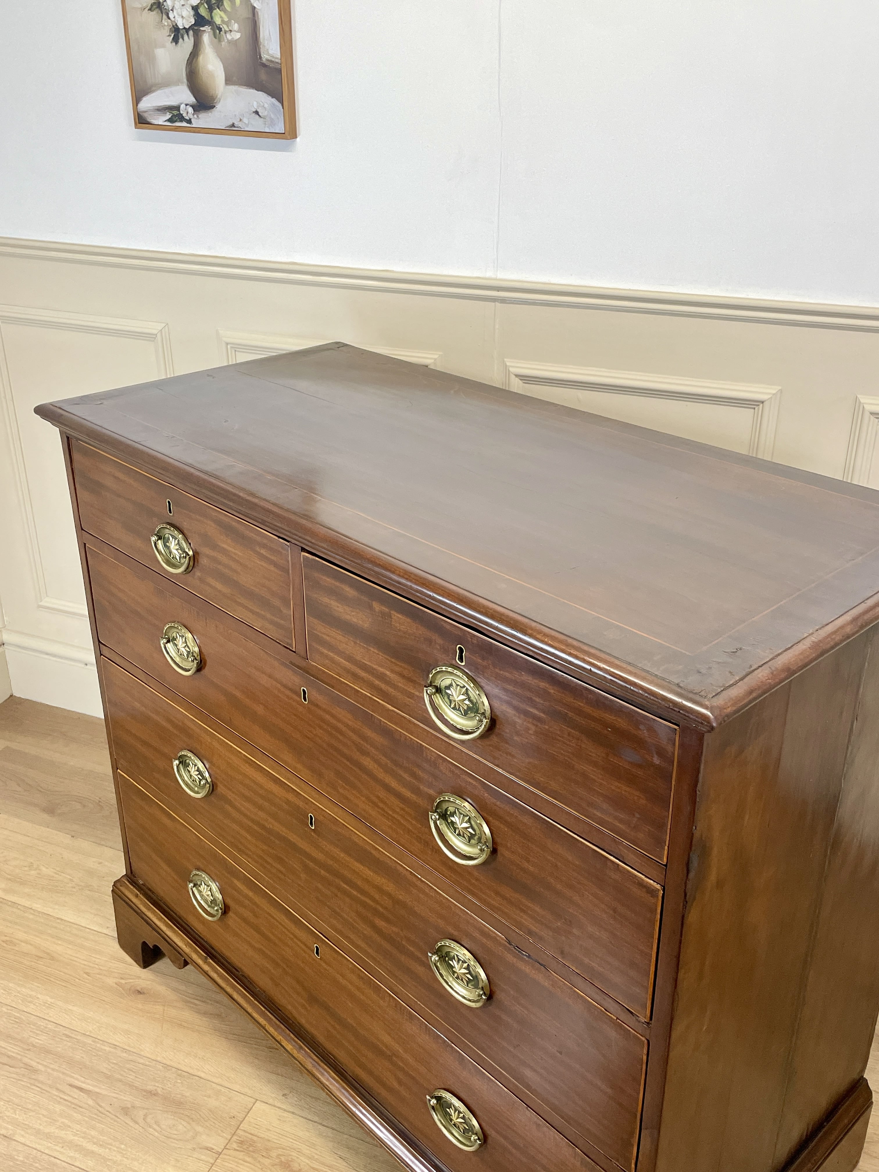 Wooden dresser with brass handles in a room with white walls and a light wood floor.
