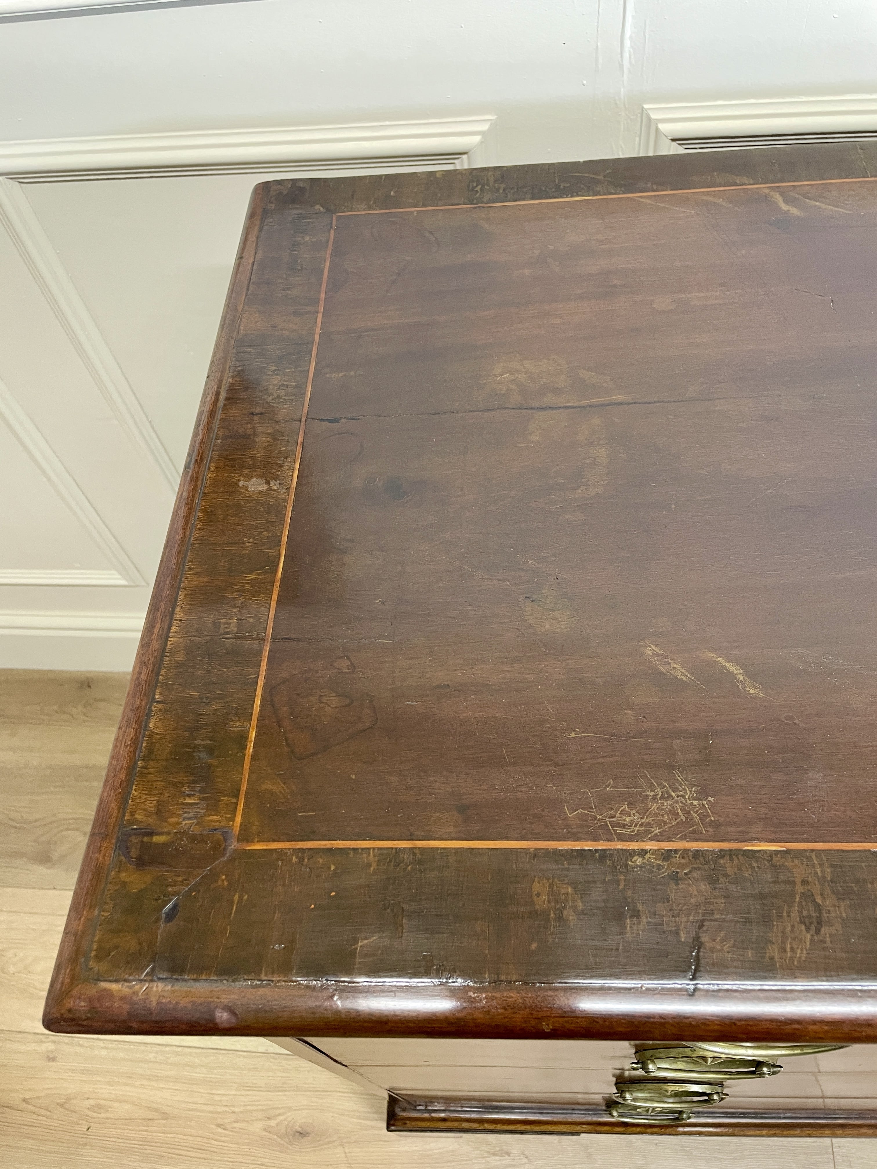 Wooden desk with a worn surface in a room with white walls and wooden floor.
