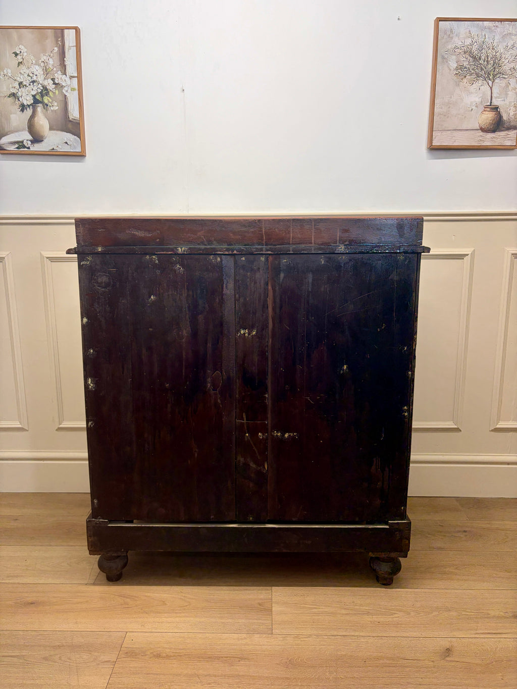 Dark wooden cabinet on wheels against a white wall with framed pictures.