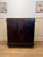 Dark wooden cabinet on wheels against a white wall with framed pictures.