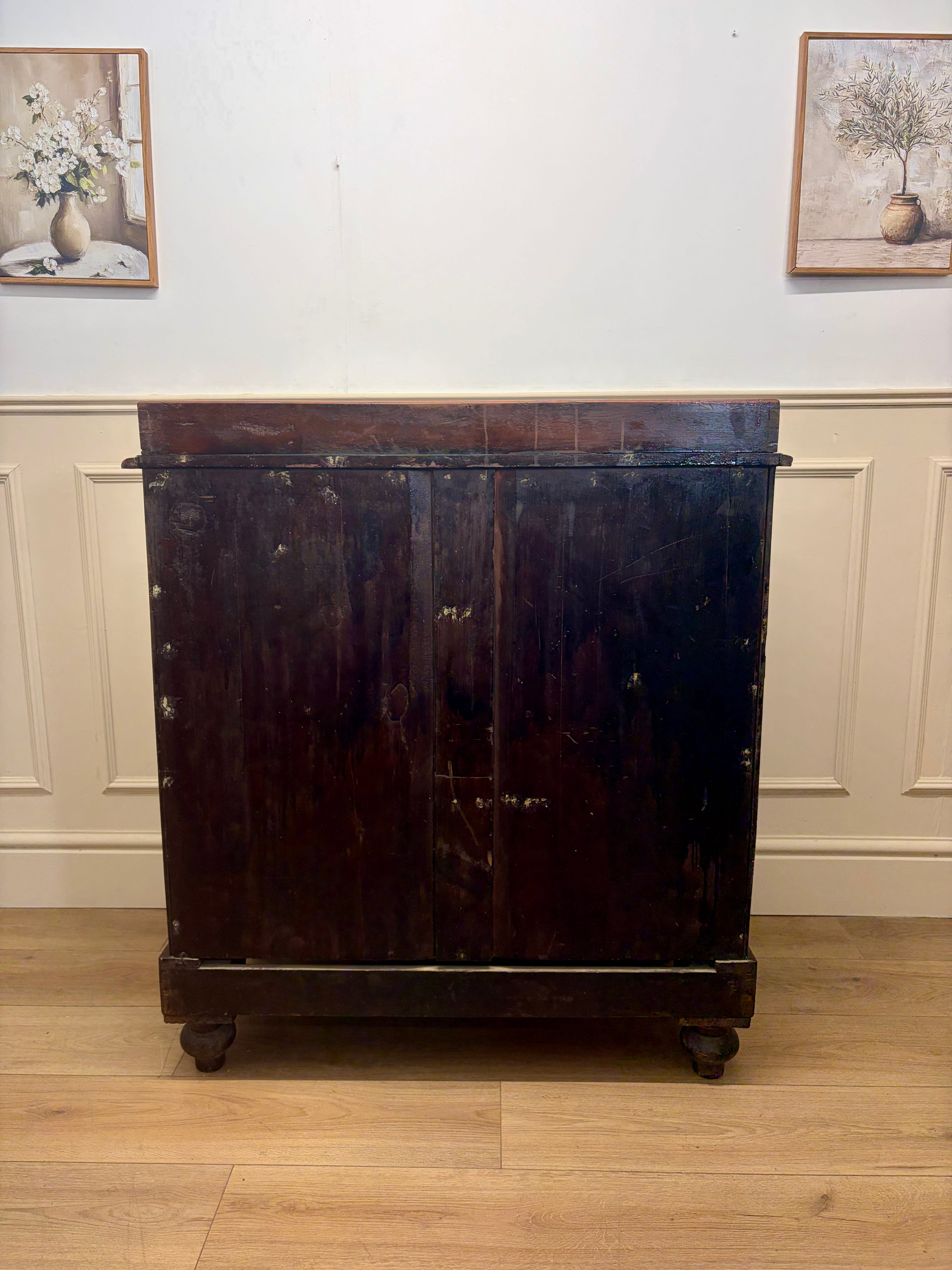 Dark wooden cabinet on wheels against a white wall with framed pictures.