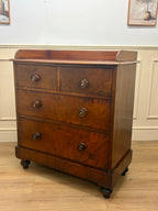 Wooden dresser with four drawers on a wooden floor against a white wall.