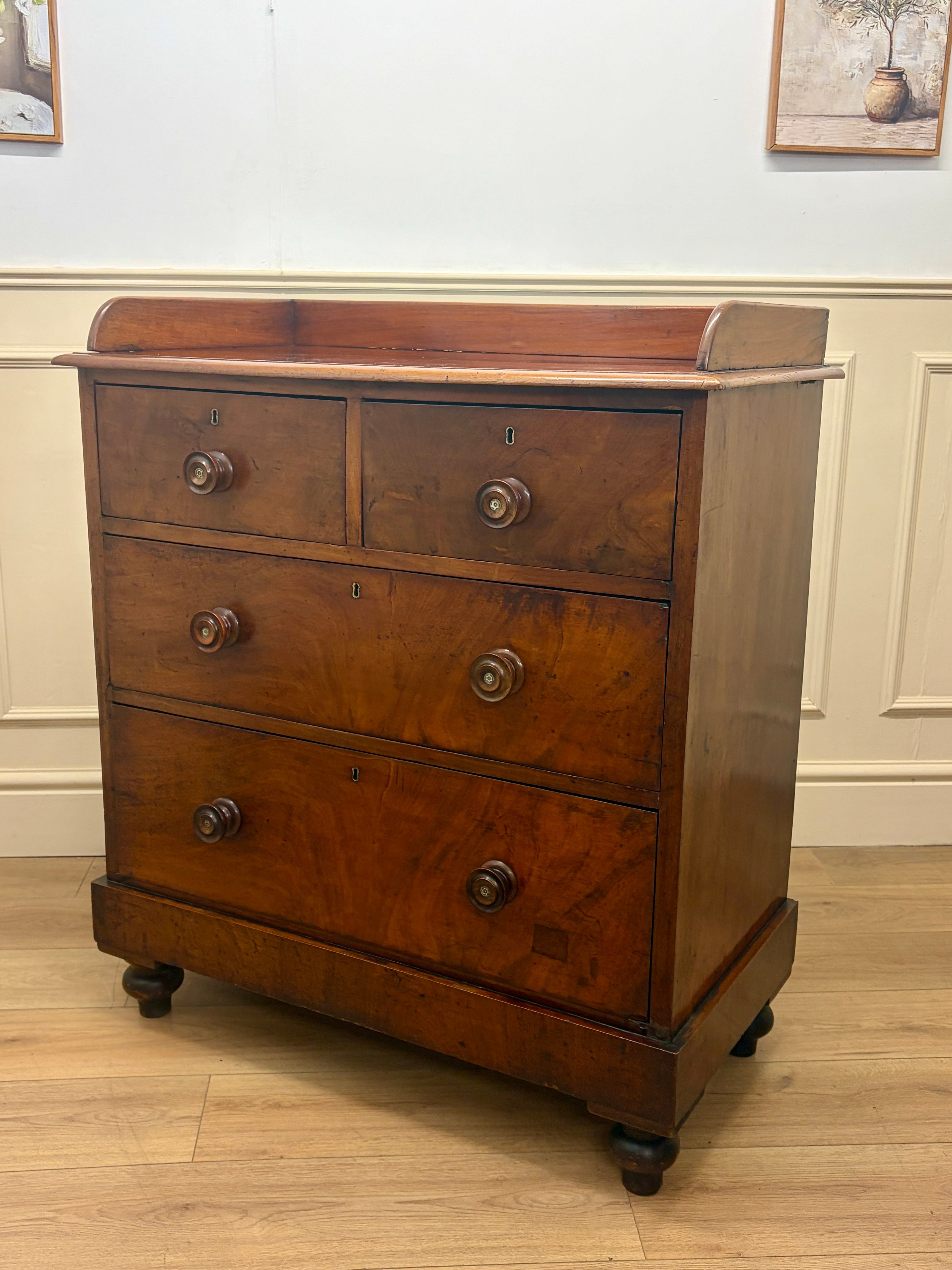 Wooden dresser with four drawers on a wooden floor against a white wall.