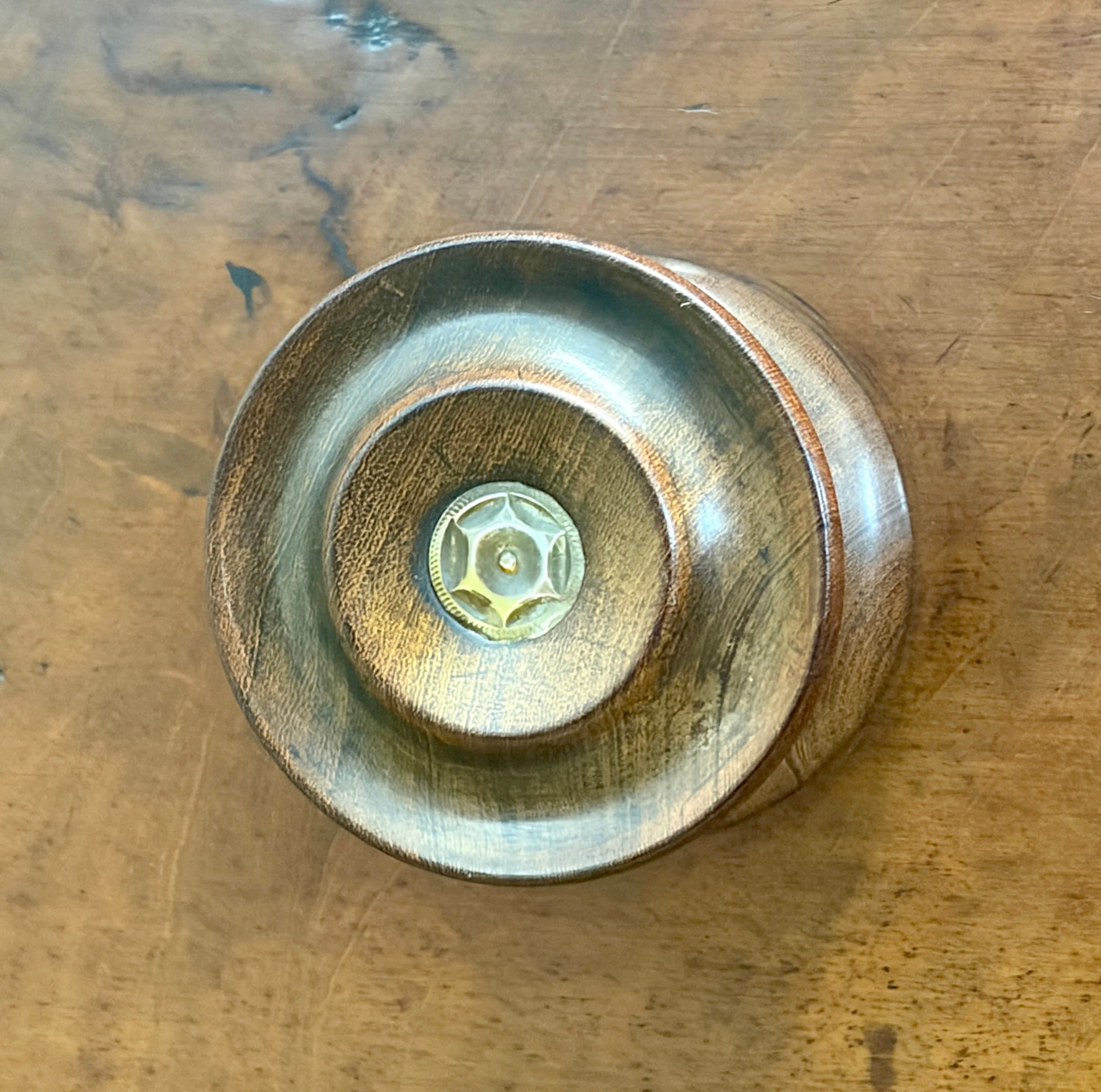 Round metallic object with central screw on a wooden surface