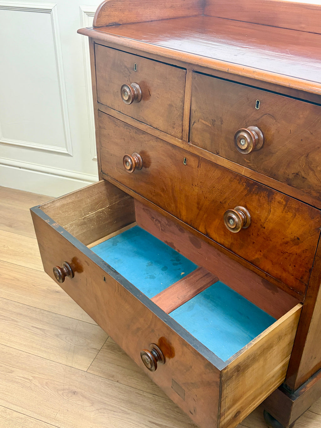 Wooden dresser with open drawer revealing a blue interior, on a wooden floor.