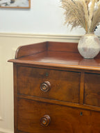 Wooden dresser with a vase of dried plants on top against a white wall.