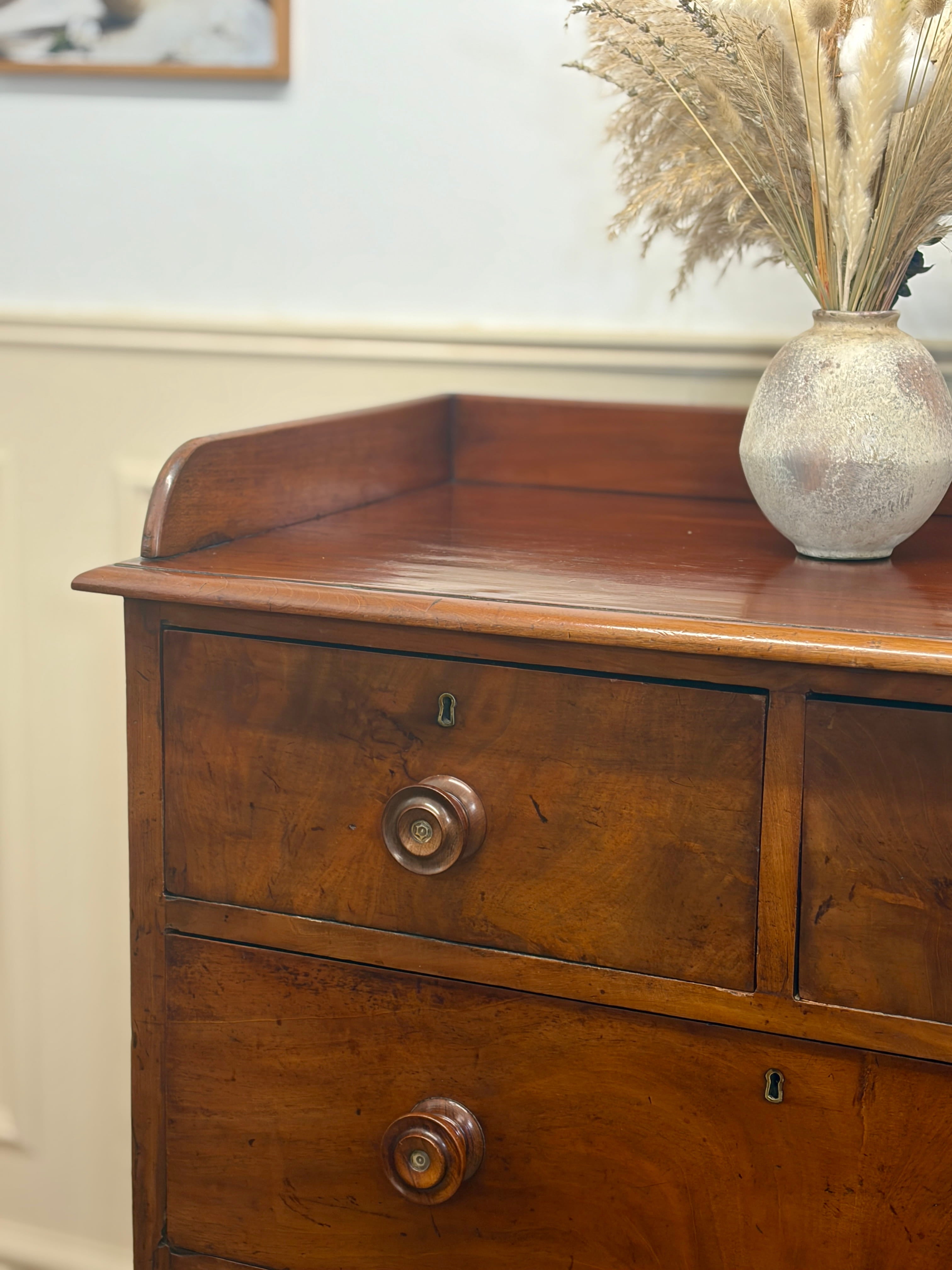 Wooden dresser with a vase of dried plants on top against a white wall.