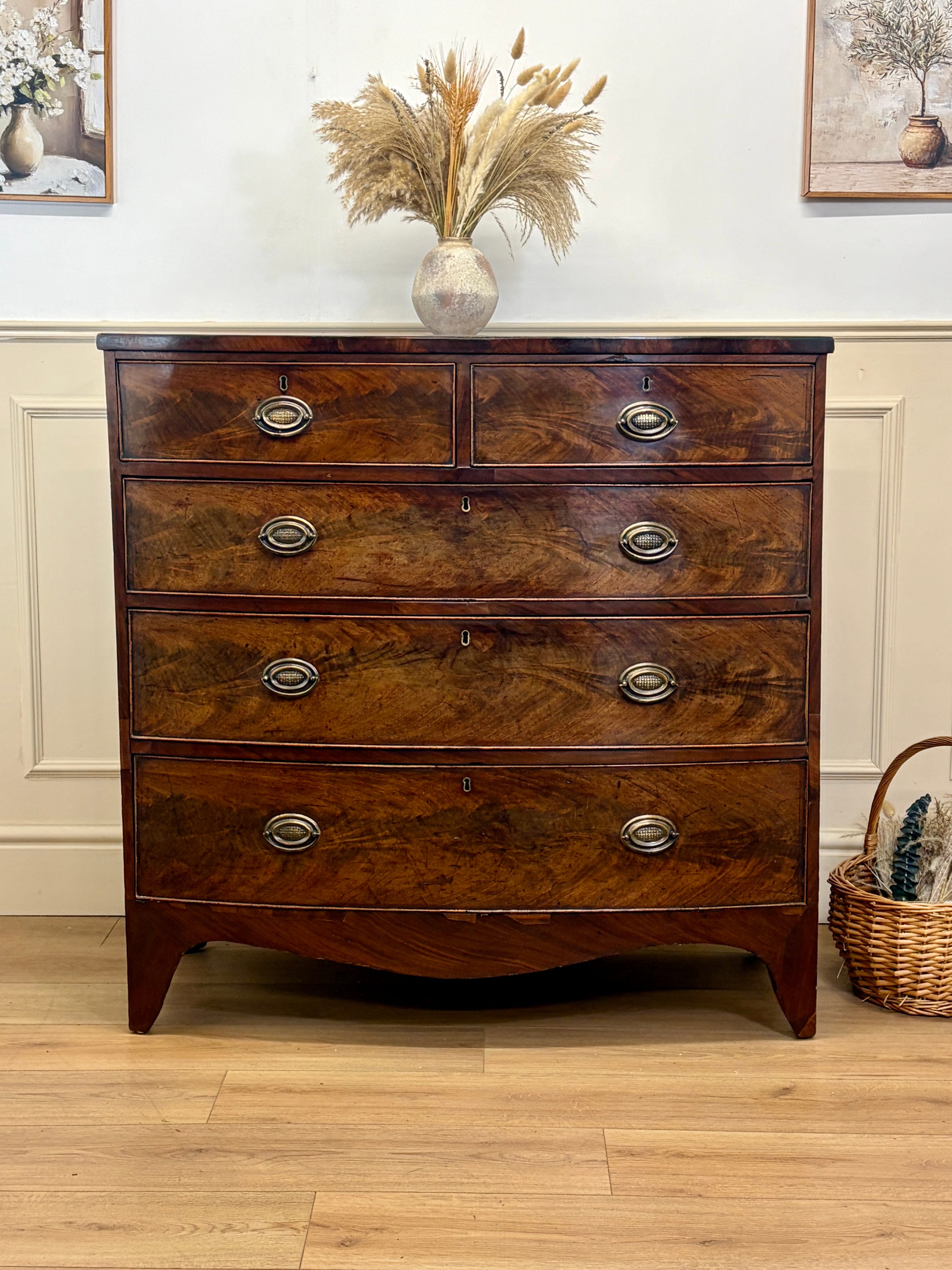 Wooden dresser with four drawers on a wooden floor, decorated with a vase and basket.