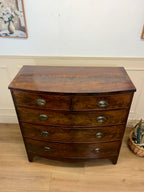Wooden dresser with curved top and four drawers on a wooden floor.