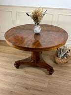 Round wooden table with a vase of dried flowers on a wooden floor.