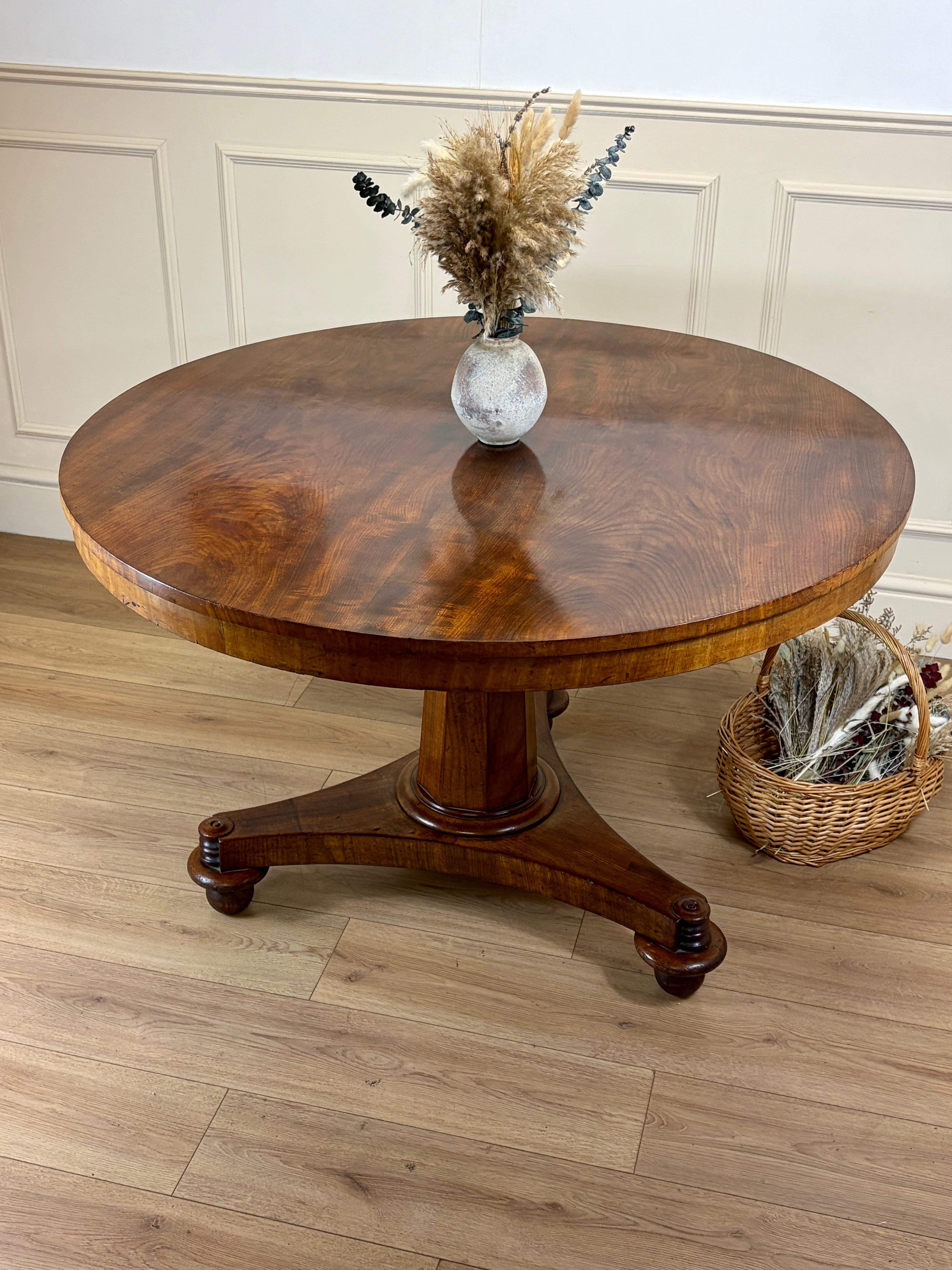 Round wooden table with a vase of dried flowers on a wooden floor.