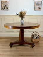 Wooden round table with a vase of flowers on a wooden floor, with two framed pictures on the wall.