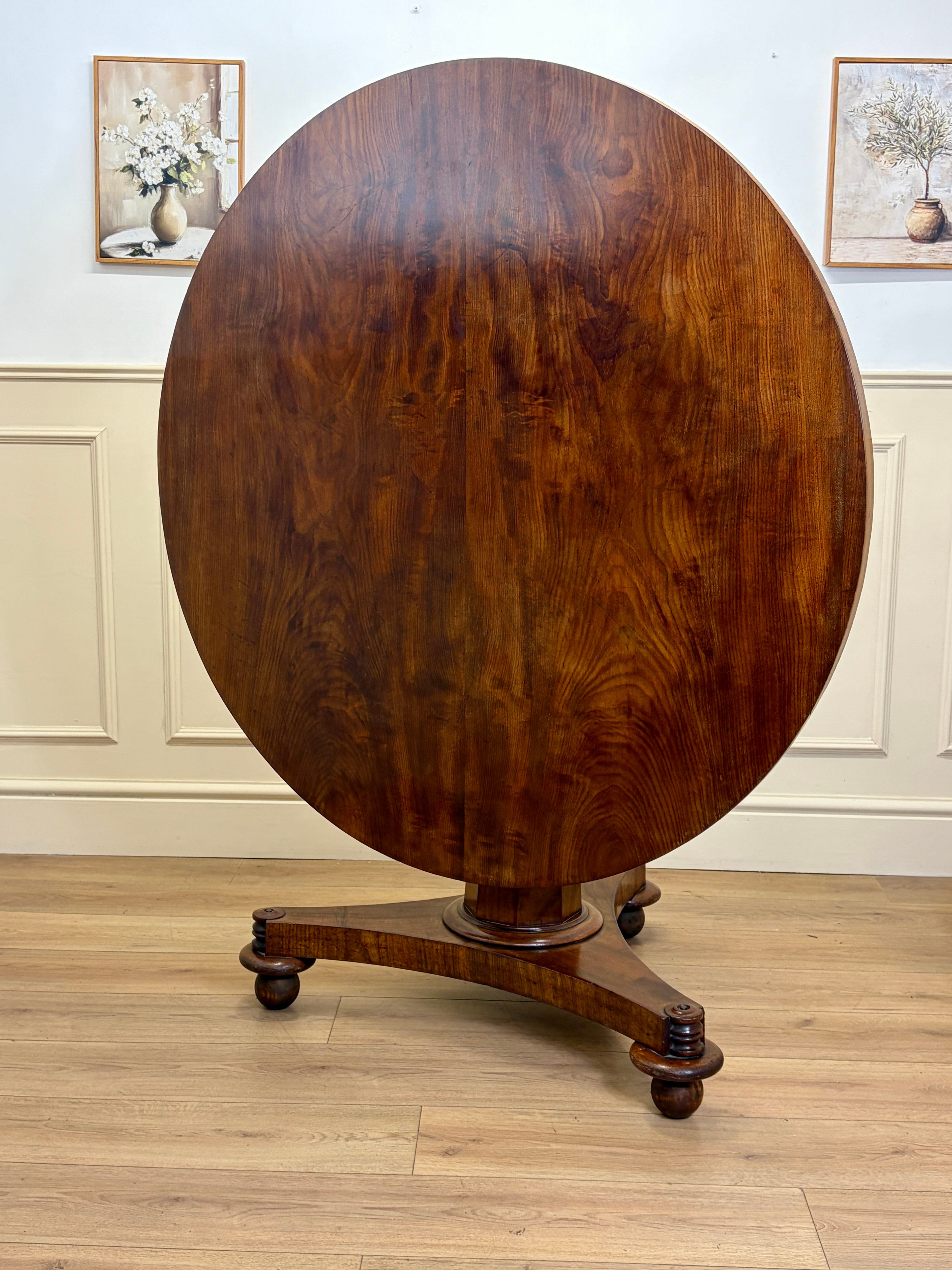 Round wooden table with a dark finish on a wooden floor with light-colored walls.