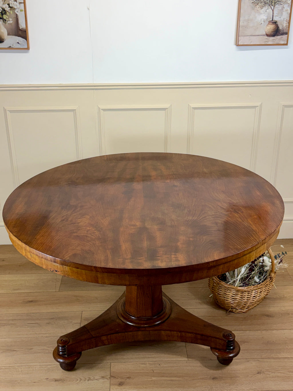 Round wooden table with a pedestal base in a room with light-colored walls and flooring.