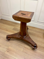 Wooden pedestal table on a wooden floor with white paneled walls.