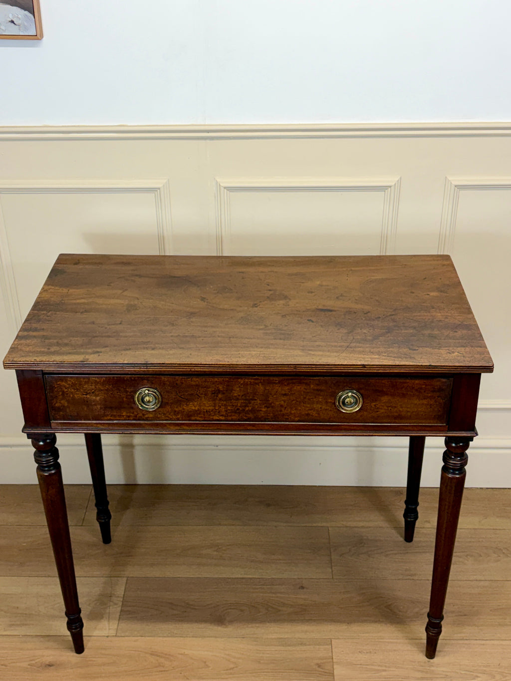 Wooden desk with a single drawer against a white wall.