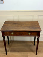 Wooden desk with a single drawer against a white wall.