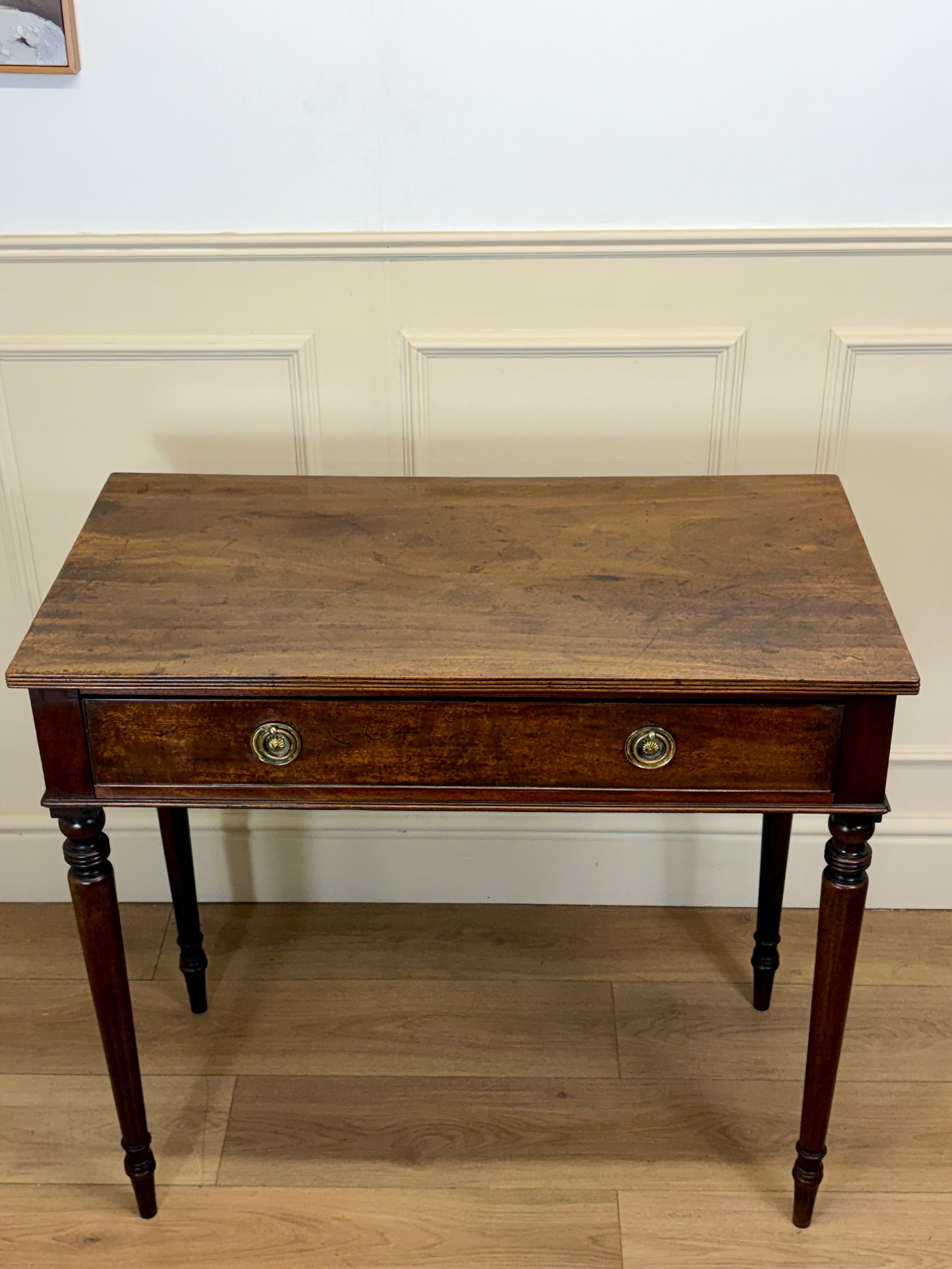 Wooden desk with a single drawer against a white wall.