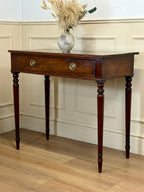 Wooden console table with a vase of dried flowers against a white paneled wall.
