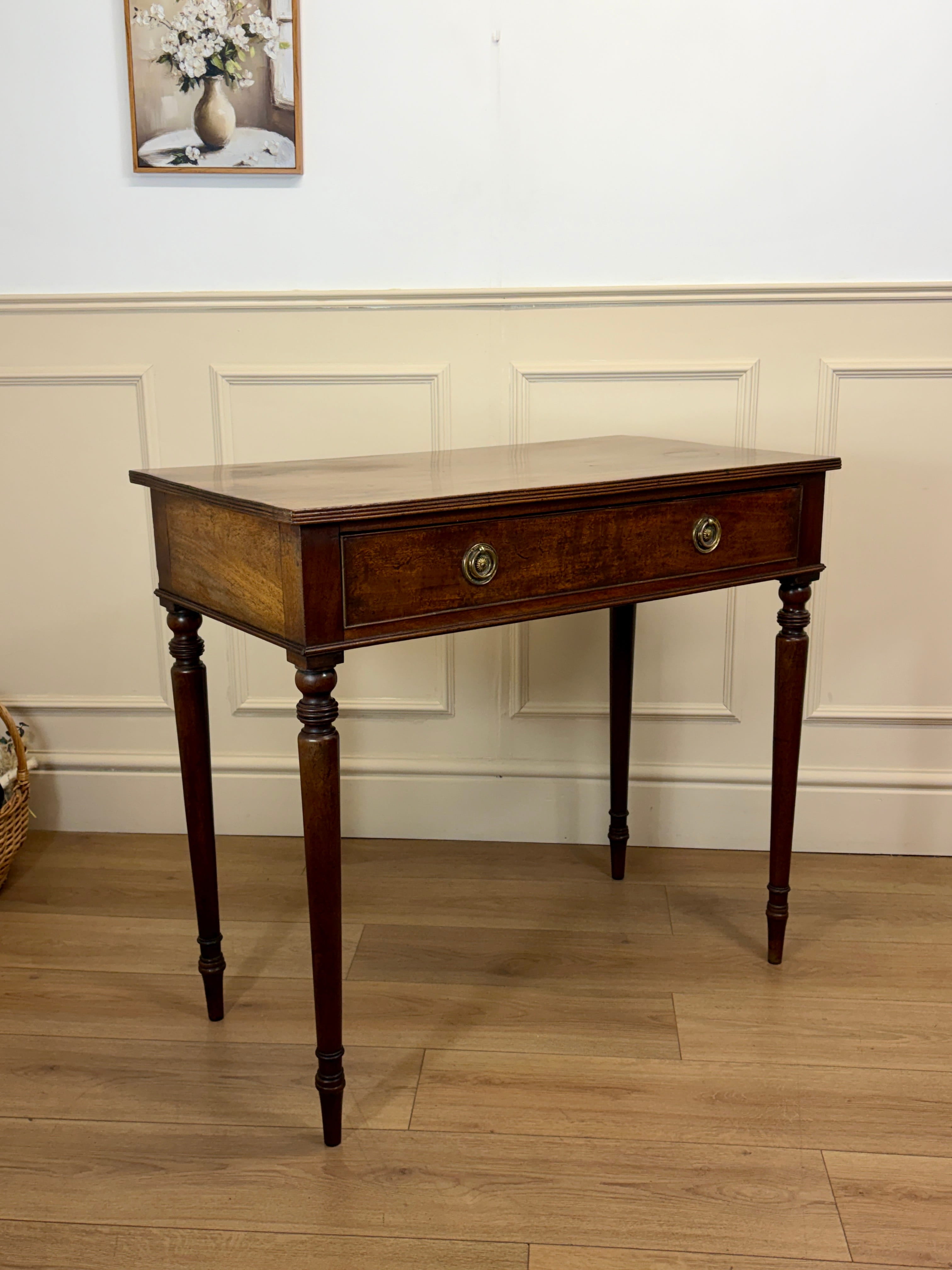 Wooden side table with a single drawer against a white paneled wall.