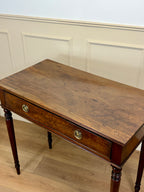 Wooden desk with a single drawer against a white paneled wall.