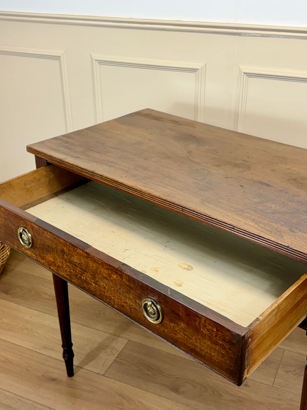 Wooden desk with a drawer open, showing a light-colored interior, against a beige wall.