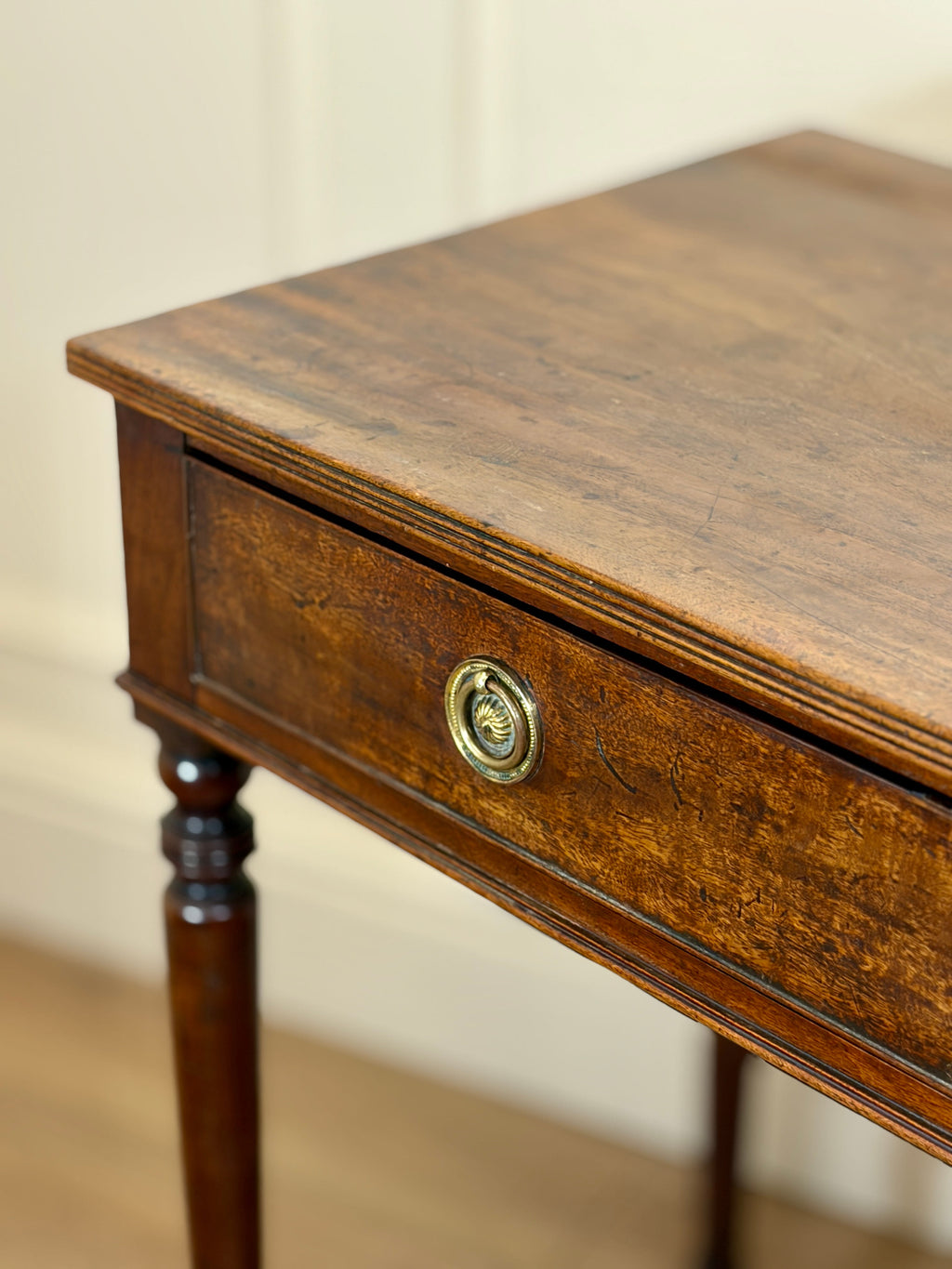 Wooden side table with a drawer and decorative knob against a beige wall.