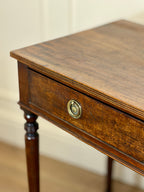 Wooden side table with a drawer and decorative knob against a beige wall.