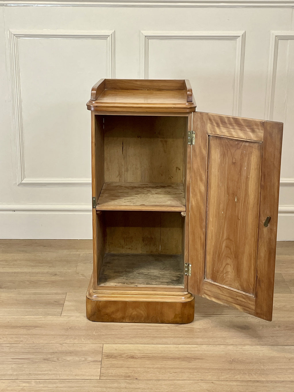 Wooden cabinet with open door on a wooden floor against a white paneled wall.