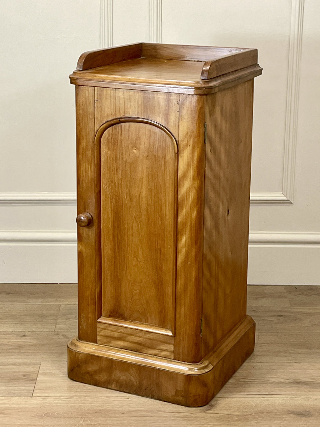 Wooden cabinet with a curved door on a wooden floor against a beige wall.