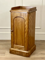 Wooden cabinet with a curved door on a wooden floor against a beige wall.