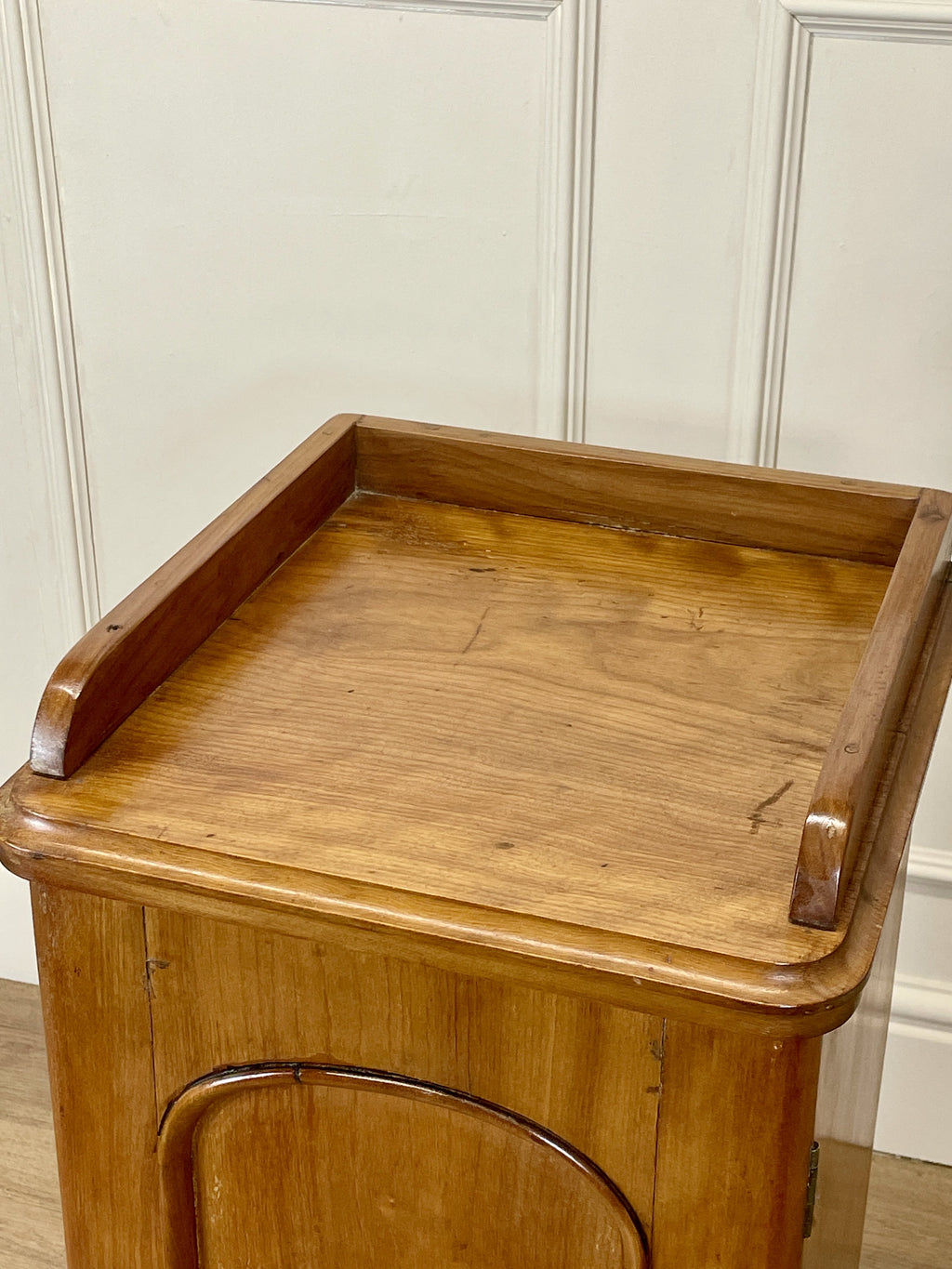 Wooden side table with a tray on top against a white paneled wall.