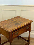 Wooden desk with a single drawer against a white paneled wall.