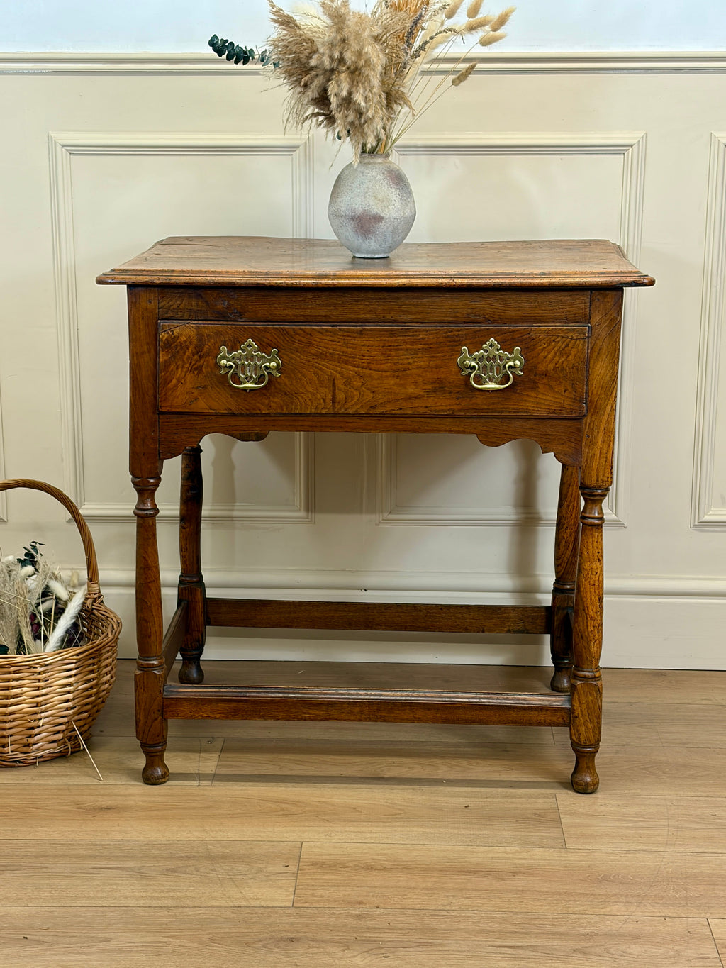 Wooden side table with a vase of dried flowers on a wooden floor.