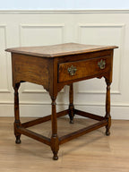 Wooden side table with a single drawer against a white paneled wall.