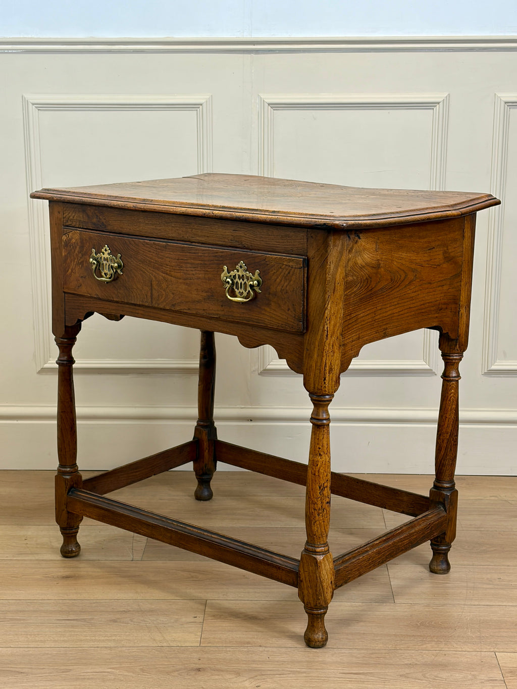 Wooden side table with a single drawer against a white paneled wall.