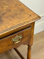 Wooden side table with a drawer and brass handle on a wooden floor.