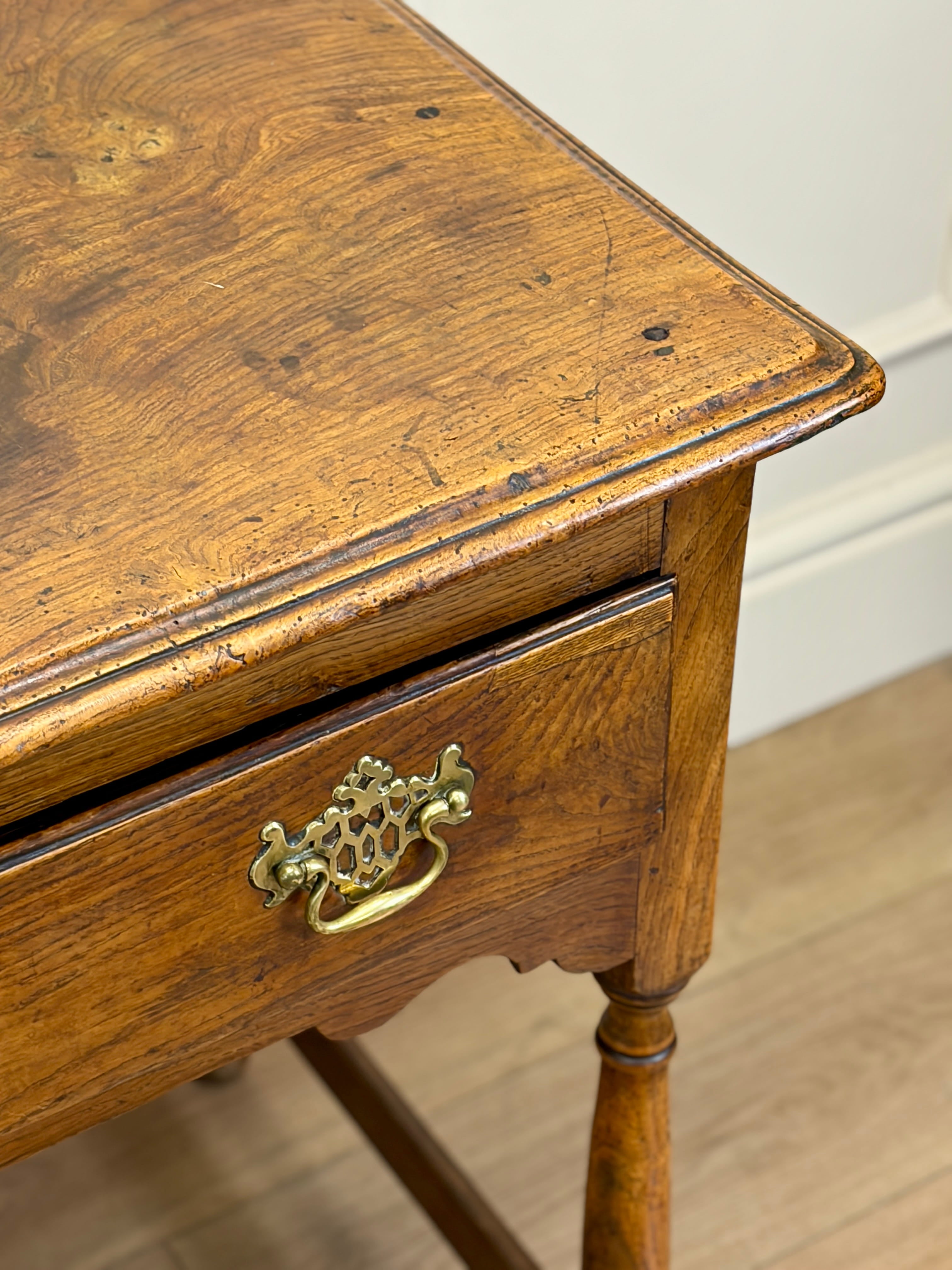 Wooden side table with a drawer and brass handle on a wooden floor.