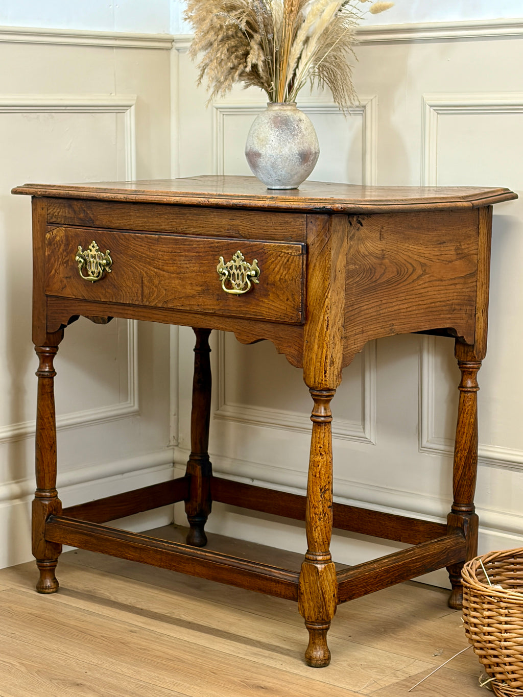 Wooden side table with a vase of dried flowers on a light-colored wall background