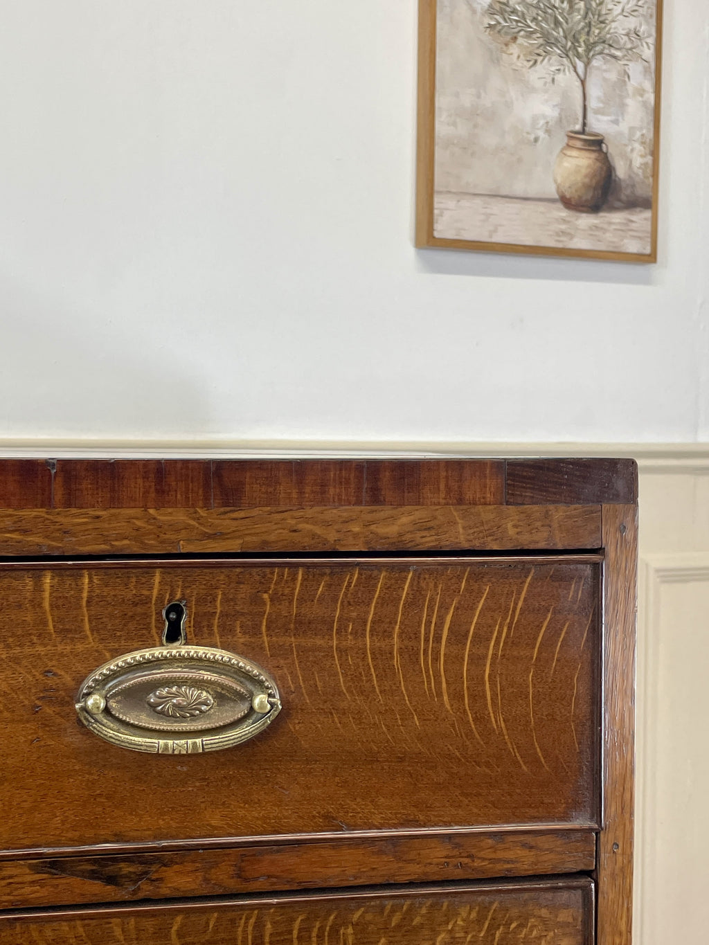 Wooden dresser with brass handle and framed artwork on the wall.