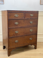 Wooden dresser with four drawers and brass handles on a wooden floor.