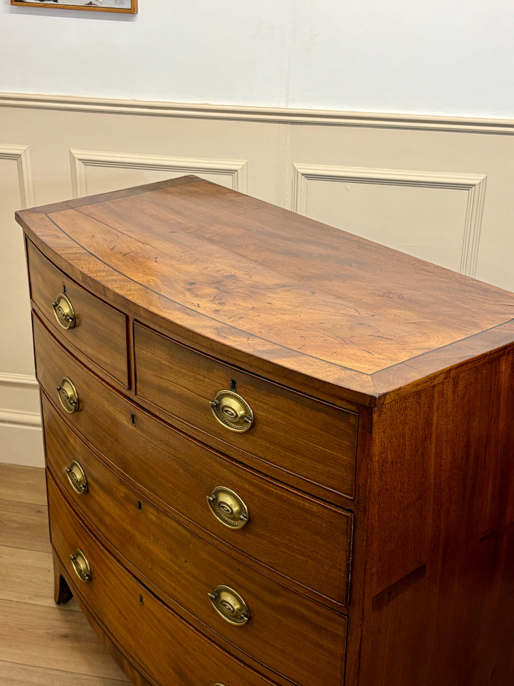 Wooden dresser with curved top and brass handles against a white wall.