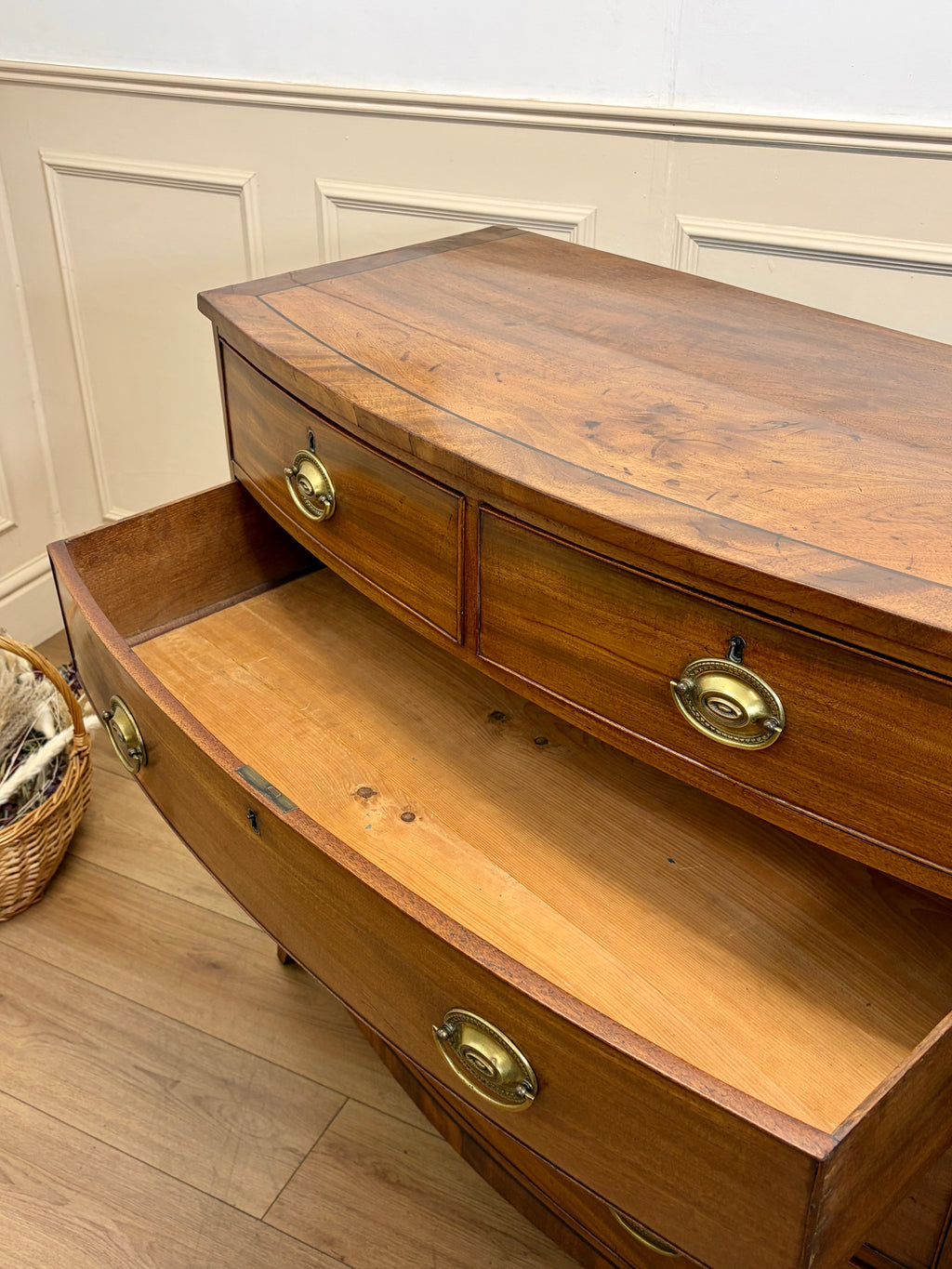 Wooden sideboard with brass handles in a room with light-colored walls and wooden floor.