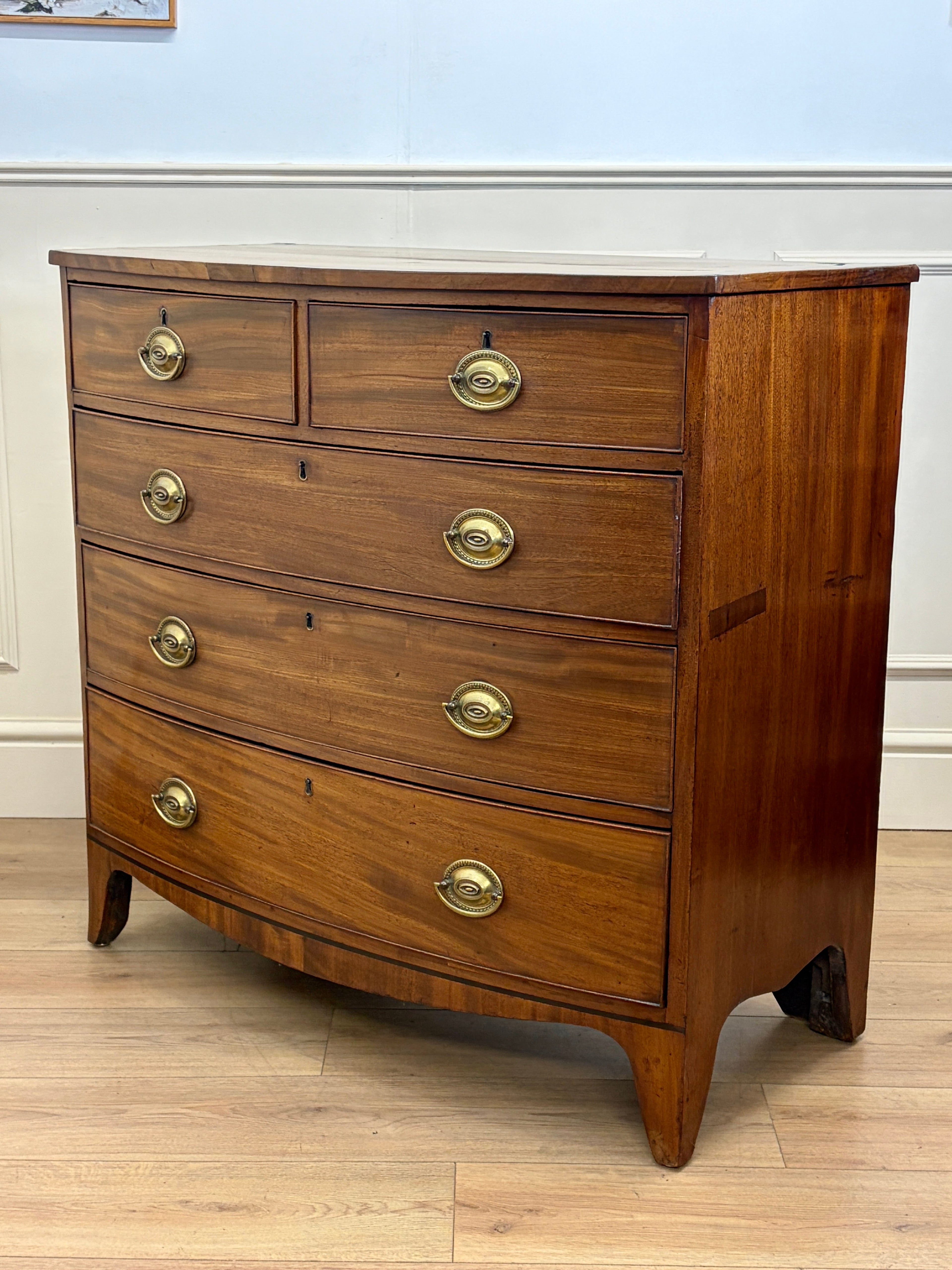 Wooden dresser with four drawers and brass handles on a wooden floor.